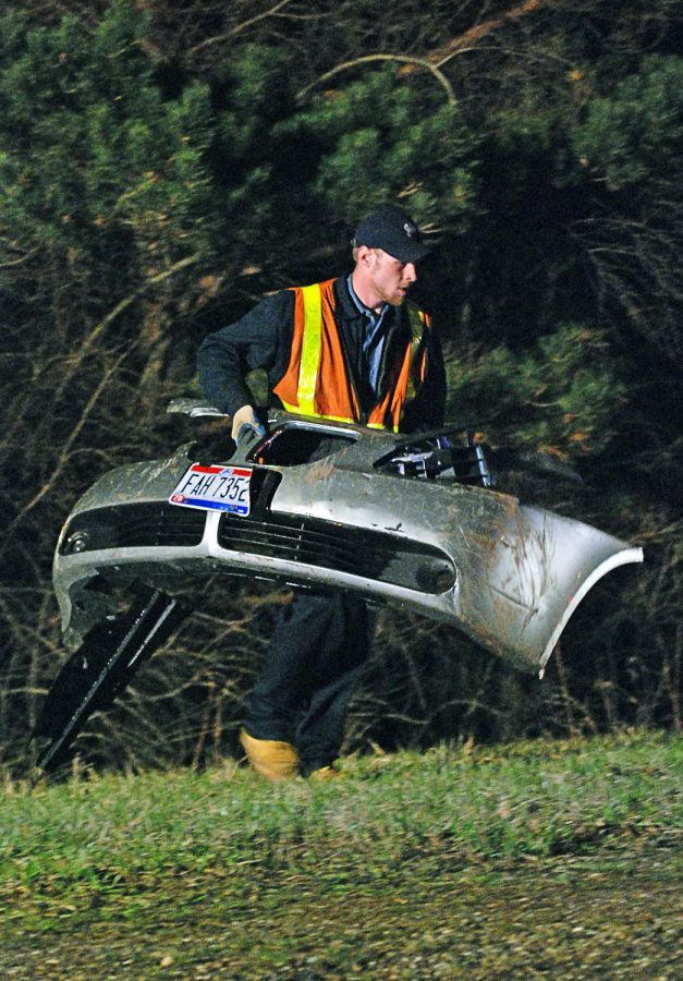 A worker from City Service Company carries the front bumper from a Pontiac G6 that went left of center on state Route 261 southbound Wednesday. Two passengers we're in the vehicle that veered off into a ditch. Only minor injuries were reported . Photo by Matt Hafley.