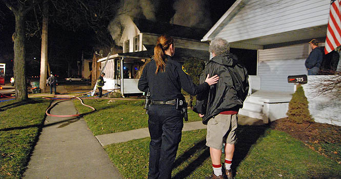 A Kent police officer comforts Eddy Milton, who lives in the lower level of a Cherry Street house that caught fire Monday night, Feb. 20. No injuries were reported. Photo by Matt Hafley.