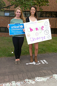 Freshmen fashion merchandising major Regina Dlwgosh and zoology major Megan Dunlap stand with signs near the UNICEF stand that has been posted on campus for several days, raising funds for efforts toward children's well being in Syria. Photo by Carolyn Pippin.