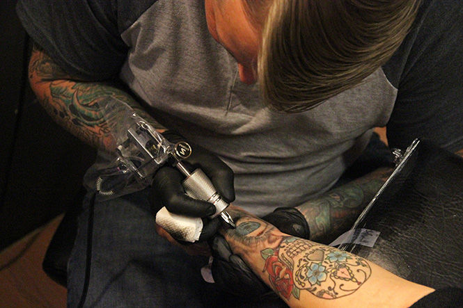 Owner Jay Miller works on fine arts major and apprentice Eliza Miller's arm piece at Crucible Tattoos on Tuesday, March 17, 2015. Eliza first got the piece when she started her apprenticeship there.