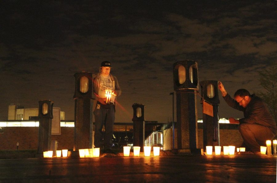 The Kent Stater Pittsburgh native Keith Pennington stands in the memorial place of William Schroeder while a by stander kneels at the edge during the May 4th Candle Light Vigil and Walk through campus on Tuesday, May 3, 2016.