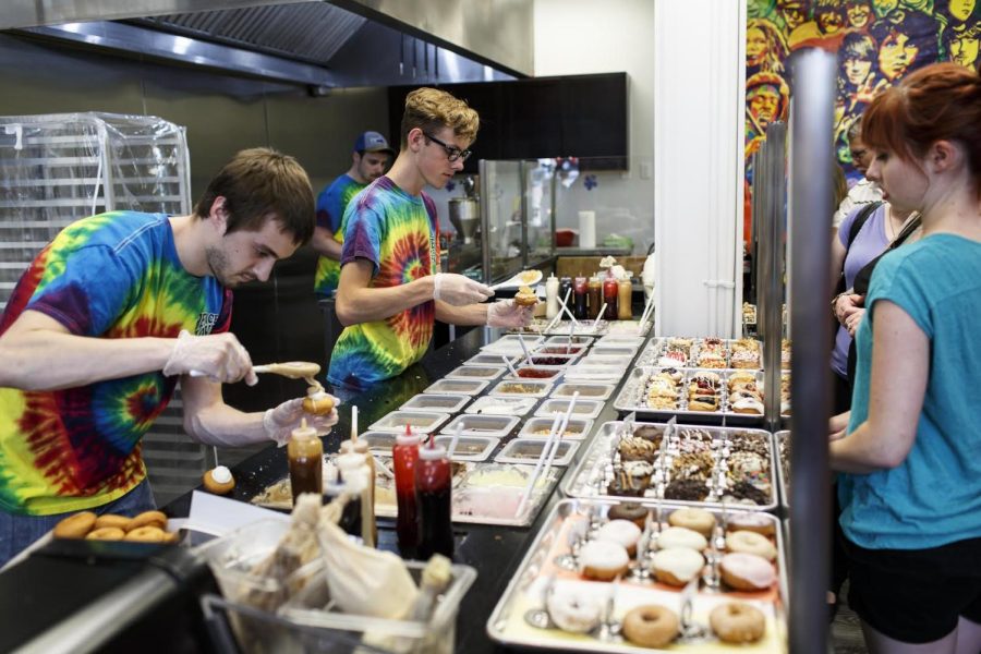 Alex Stayer (left) and Donnie Cuthbert (center) add the finishing touches to customers’ orders at Peace, Love &amp; Little Donuts in downtown Kent on Friday, June 10, 2016.