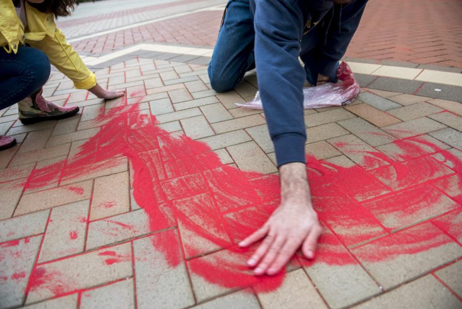 Vice President of Kent's International Justice Mission student organization Delaney Cordova and architecture sophomore Nathaniel Williams spread red sand into the cracks of the K in the middle of Risman Plaza Wednesday March 1. The Red Sand Project was started by artist Molly Goochman to bring awareness to the human trafficking epidemic.