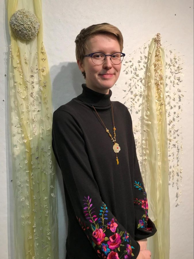 First-year graduate student Meagan Smith poses in front of two pieces of her textile work, “Untitled.” Smith said she draws inspiration from her time as a competitive swimmer.“A pool has a lot of verticality and linear elements and repetition on the bottom (with) the tiles,” Smith said. “And I think that’s a strong influence for my work, body memory and linear stretching of the body. I’m looking at a lot of order and systems that connect to the body.” 