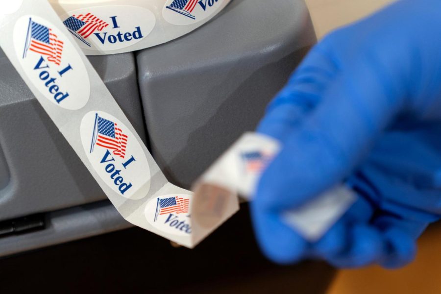 Poll worker Sheila Hawkes removes an "I Voted" sticker to hand to a voter at an early voting center at Ida B. Wells Middle School, Thursday, Oct. 29, 2020, in Washington. (AP Photo/Jacquelyn Martin)