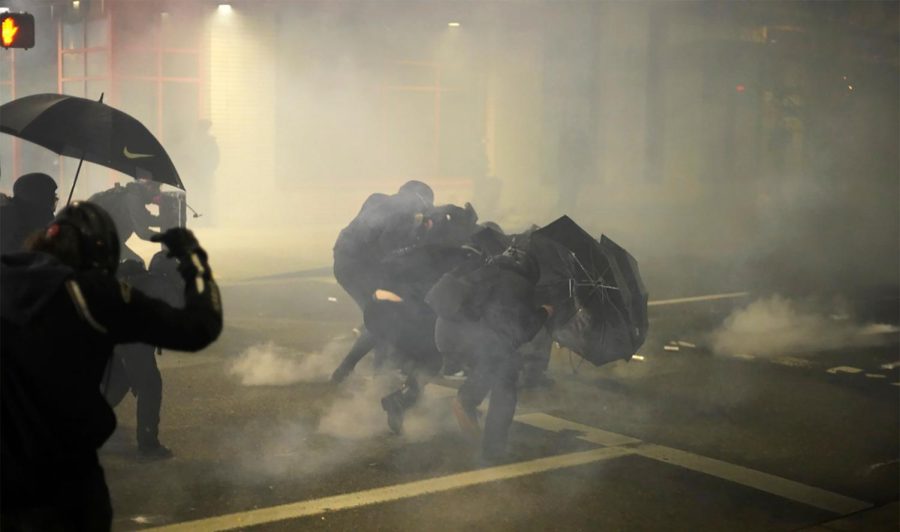 A group of protesters shield themselves from chemical irritants as they demonstrate Wednesday evening, Jan. 20, 2021, outside the U.S. Immigrations and Customs Enforcement (ICE) building in Portland, Ore. (Assfault Pirates via AP)