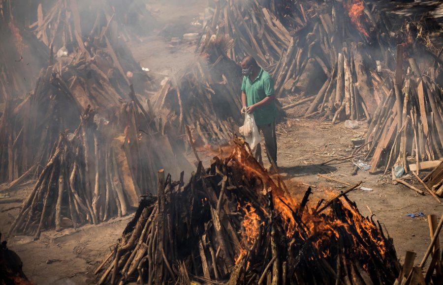 NEW DELHI, INDIA - APRIL 24: A man performs the last rites of his relative who died of the Covid-19 coronavirus disease as other funeral pyres are seen burning during a mass cremation held at a crematorium on April 24, 2021 in New Delhi, India. With recorded cases crossing 300,000 a day, India has more than 2 million active cases of Covid-19, the second-highest number in the world after the U.S. A new wave of the pandemic has totally overwhelmed the country's healthcare services and has caused crematoriums to operate day and night as the number of victims continues to spiral out of control. (Photo by Anindito Mukherjee/Getty Images)