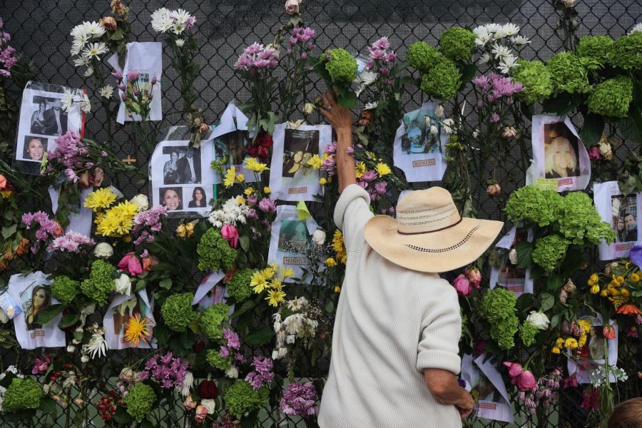 SURFSIDE, FLORIDA - JUNE 28: A person adds flowers to a memorial that has pictures of some of the missing from the partially collapsed 12-story Champlain Towers South condo building on June 28, 2021 in Surfside, Florida. The pictures were placed on the fence as loved ones try to find them. Over one hundred people are being reported missing as the search-and-rescue effort continues. (Photo by Joe Raedle/Getty Images)