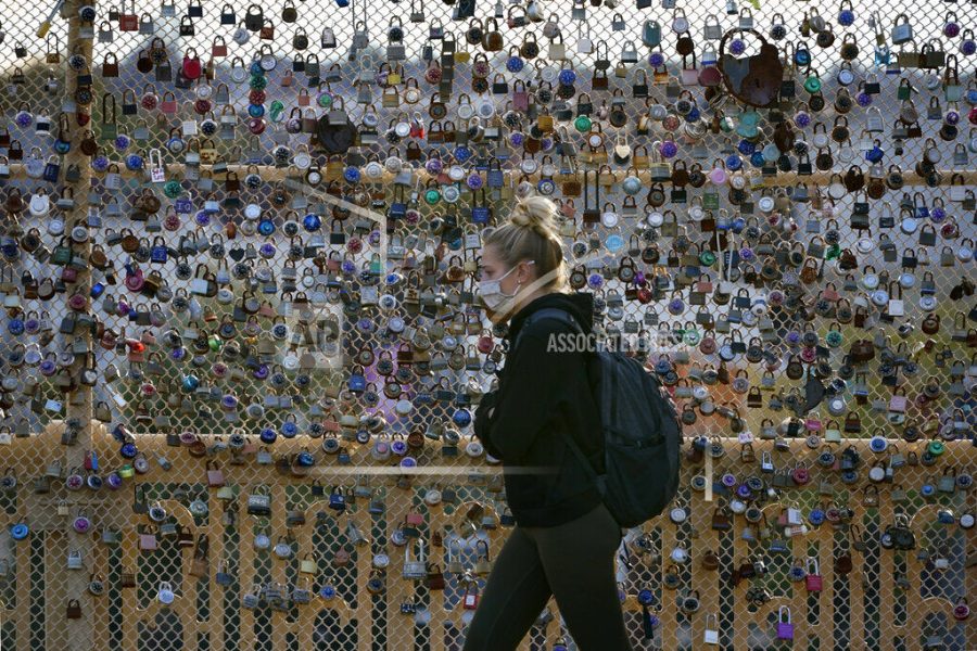 FILE - Locks cover the fence on the Love Bridge in the Oakland neighborhood of Pittsburgh as a person walks by Nov. 3, 2021. A poll from MTV Entertainment Group and The Associated Press-NORC Center for Public Affairs Research finds that Americans ages 13 through 56 think the pandemic made parts of their lives harder, but Gen Z reported higher levels of disruption to their education and dating lives. (AP Photo/Gene J. Puskar, File)