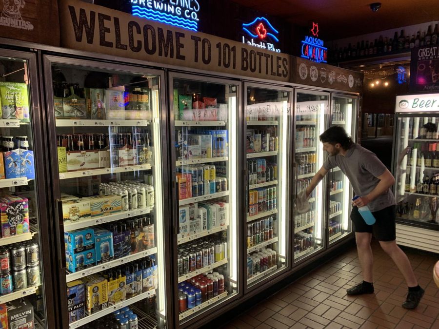 Employee Kyle Lambert wipes down the glass on the beer display case at 101 Bottles of Beer on the Wall. Lambert has worked at the bar since November and said he's learned a lot about beer and wine since taking the position.