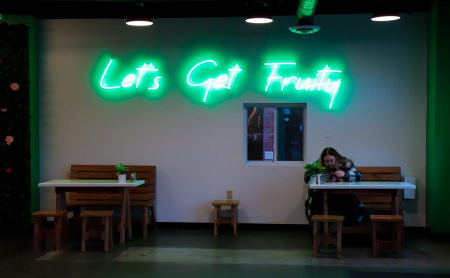 A student eats their fruit bowl under the neon sign at Fruit Stand in downtown Kent.  