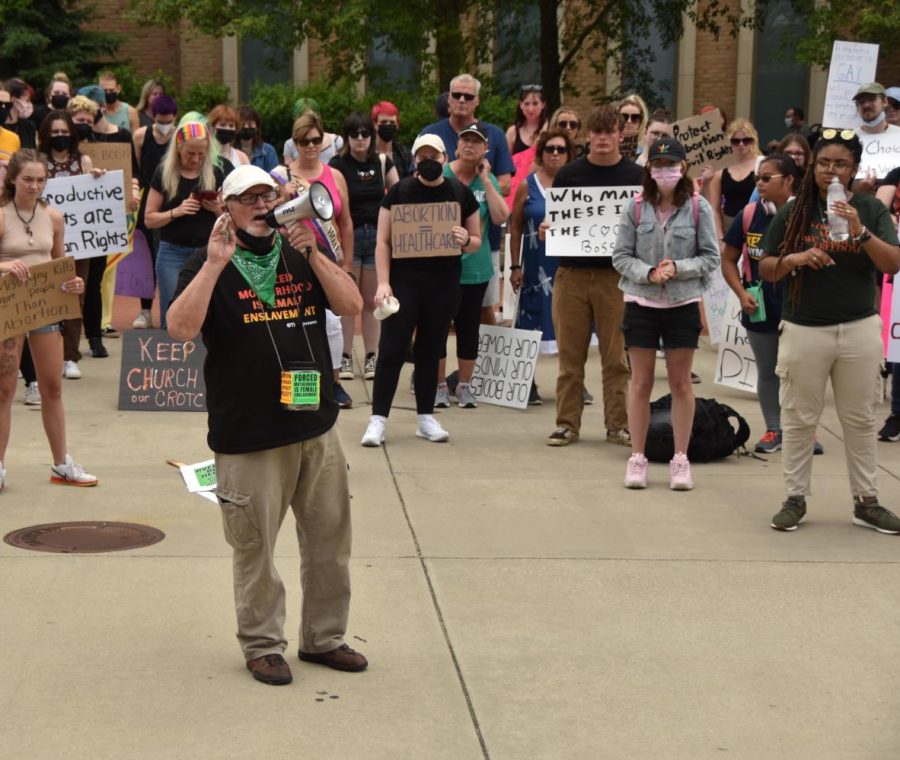 A representative from Rise Up 4 Abortion Rights urges listeners to take action, including wearing a green bandana to represent Latinx people who are affected by the overturning of Roe v. Wade.