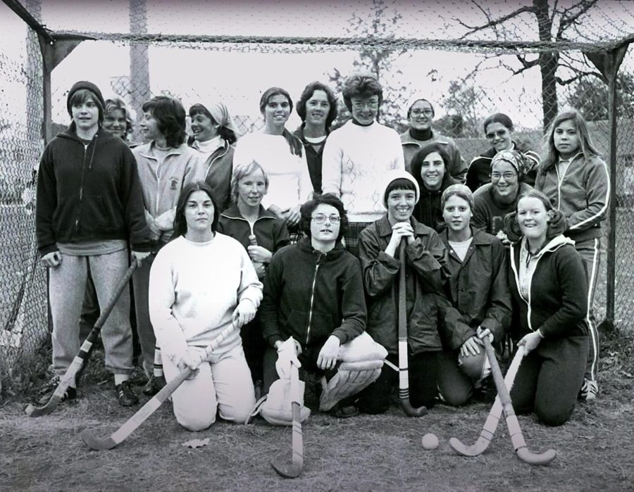 Kent State's 1975 field hockey team poses with Coach Judy Devine, center back, in front of a homemade goal cage. Each athlete is wearing her own practice gear and holding hockey sticks that were borrowed from the physical education inventory. 