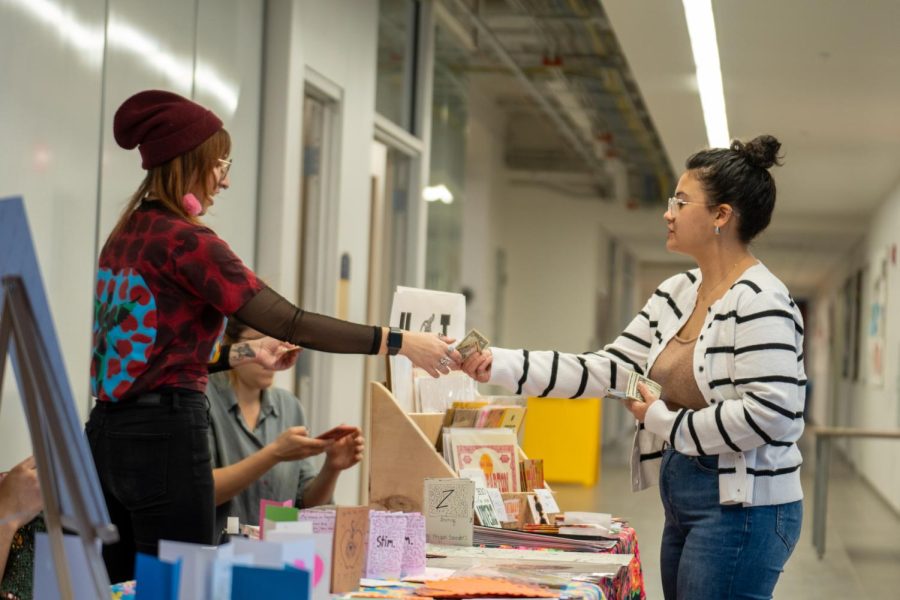 Echo Davis, who majors in cermaics, purchases a variety of cards and stickers from Brittany Gorelick at the art sale on Feb. 10, 2023.