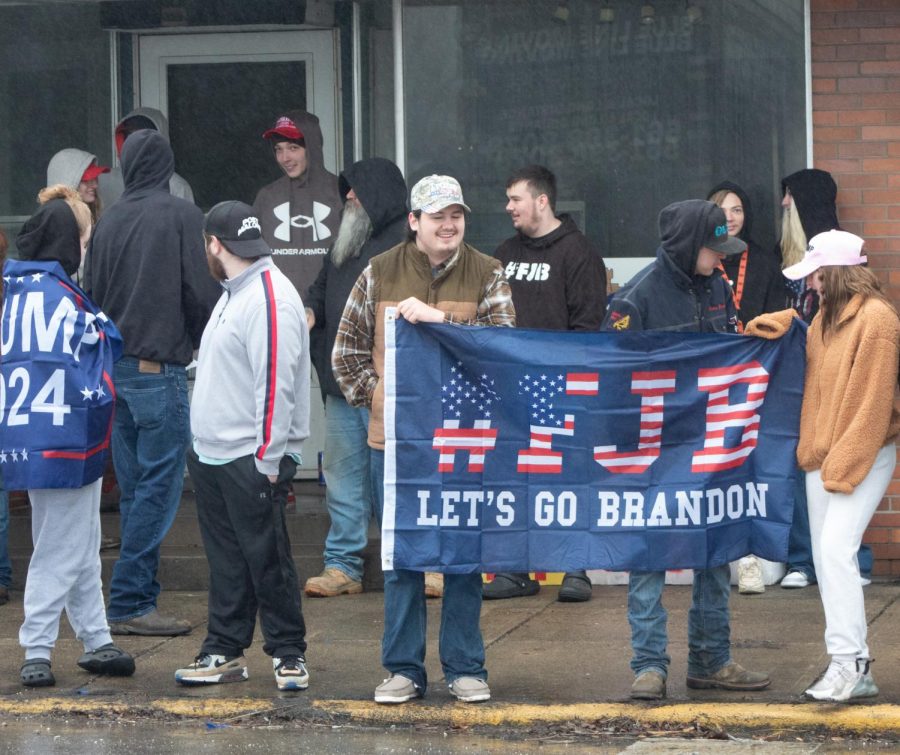 East Palestine residents and visitors stand on North Market Street on Feb. 22, holding a flag that reads "#FJB Let's Go Brandon." Attendees were waiting outside for former president Donald Trump's visit since 9 a.m.