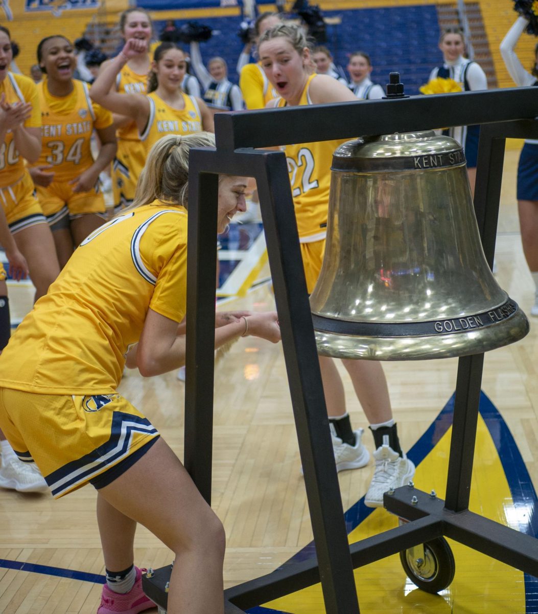 Redshirt sophomore guard Kaley Perkins rings the Starner Victory Bell, with graduate student guard Abby Ogle and the team cheering her on, after following the Golden Flashes' 109-31 win over LaRoche on Dec. 30, 2023. Perkins, a transfer from Oklahoma, netted her season high in minutes, rebounds, blocks and made field goals in the game and was selected by the team to ring the bell.