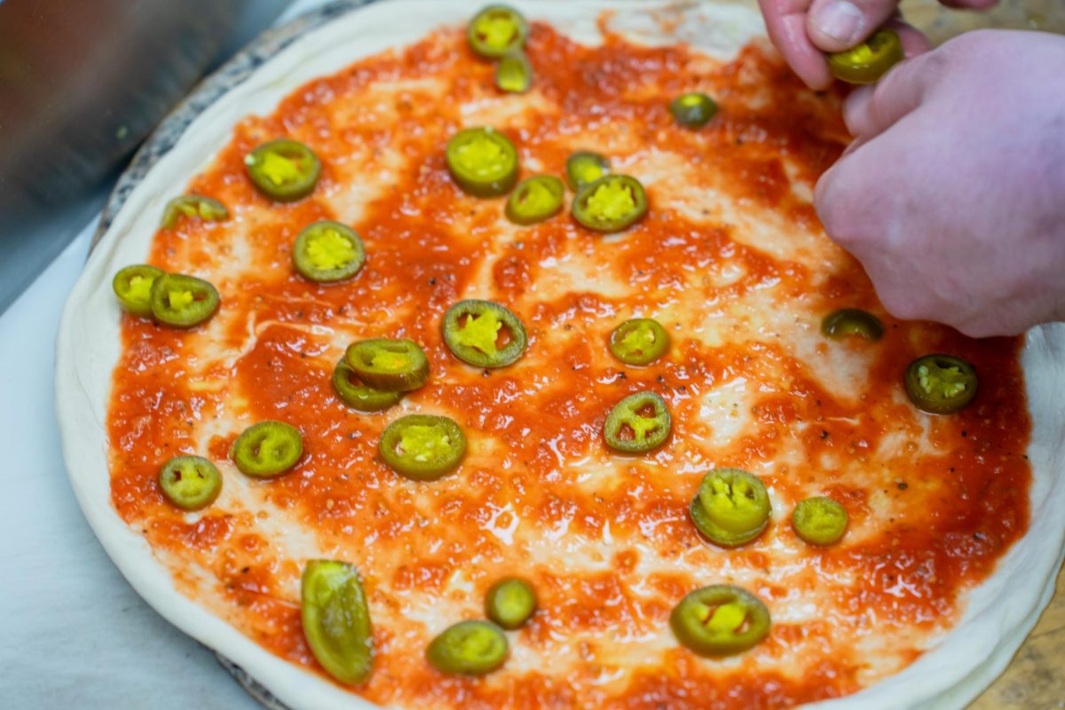 A worker at Lucci's Place builds a customer's made-to-order pizza before putting it into the oven.