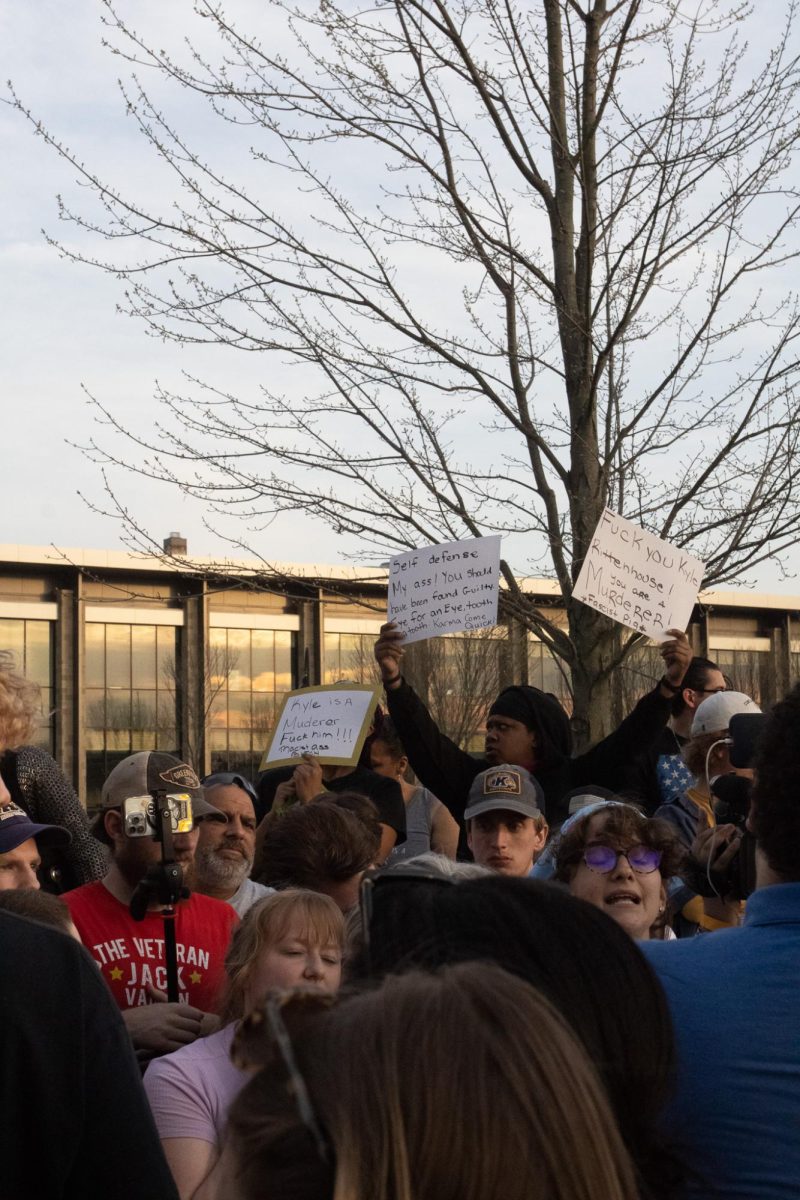 A protestor holds up signs above the crowd of fellow protestors and The Rittenhouse Recap on April 16, 2024.