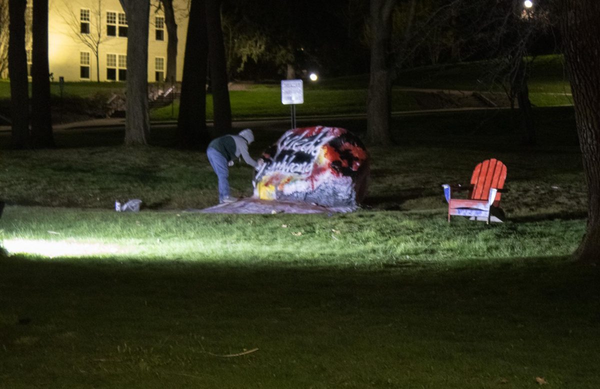 A sisguised figure spray paints the message 'Kyle did nothing wrong' on Kent State's campus rock April 15, 2024.