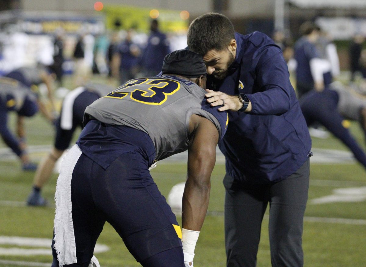 Graduate student cornerback Naim Muhammad stretched while getting a pre-game talk from a coach before their game against Ohio University on November 6,2024.  