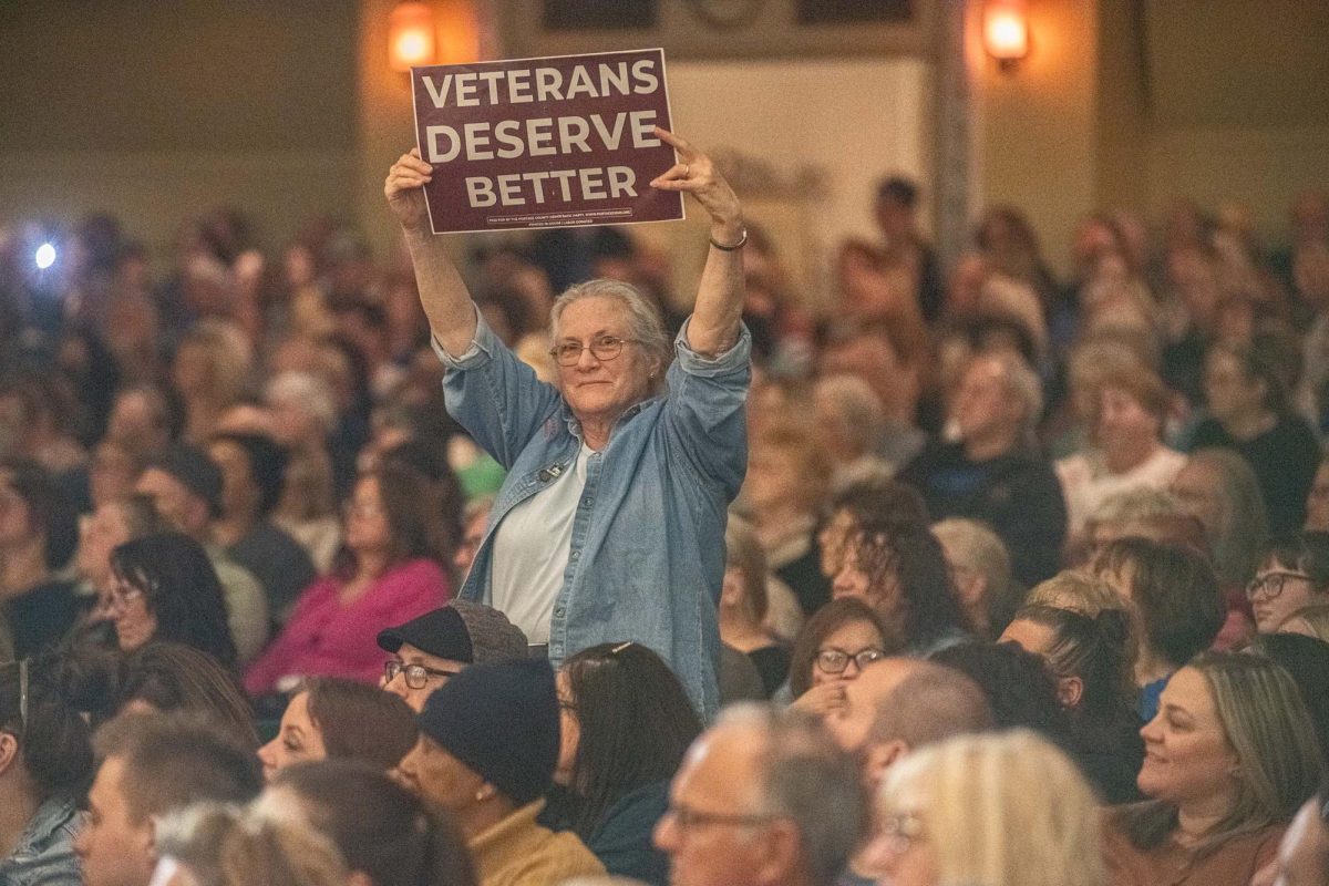 Attendees hold up signs during Tim Walz's town hall on Monday, April 7th, 2025