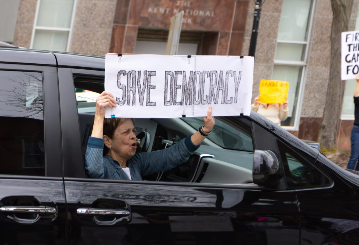 A woman holds a "Save Democracy" sign outside of her car in support of the Hands Off Protest in Downtown Kent, April 5, 2025.