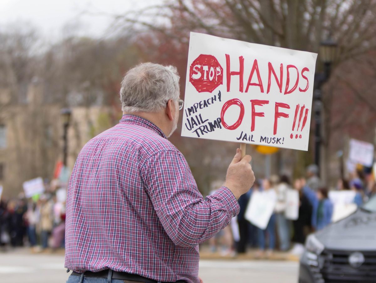 Kent resident Don Rankin crosses East Main Street with a sign protesting the Trump Administration at the Hands Off protest, April 5, 2025.