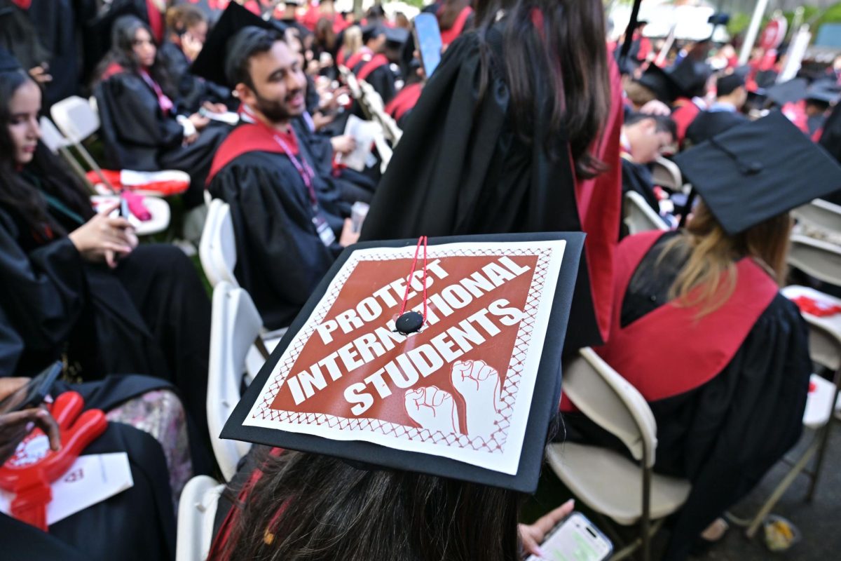 A Harvard University graduate with a message in support of international students on her mortarboard sits with fellow students at the start of commencement exercises at Harvard University in Harvard Yard, May 29, in Cambridge, MA.