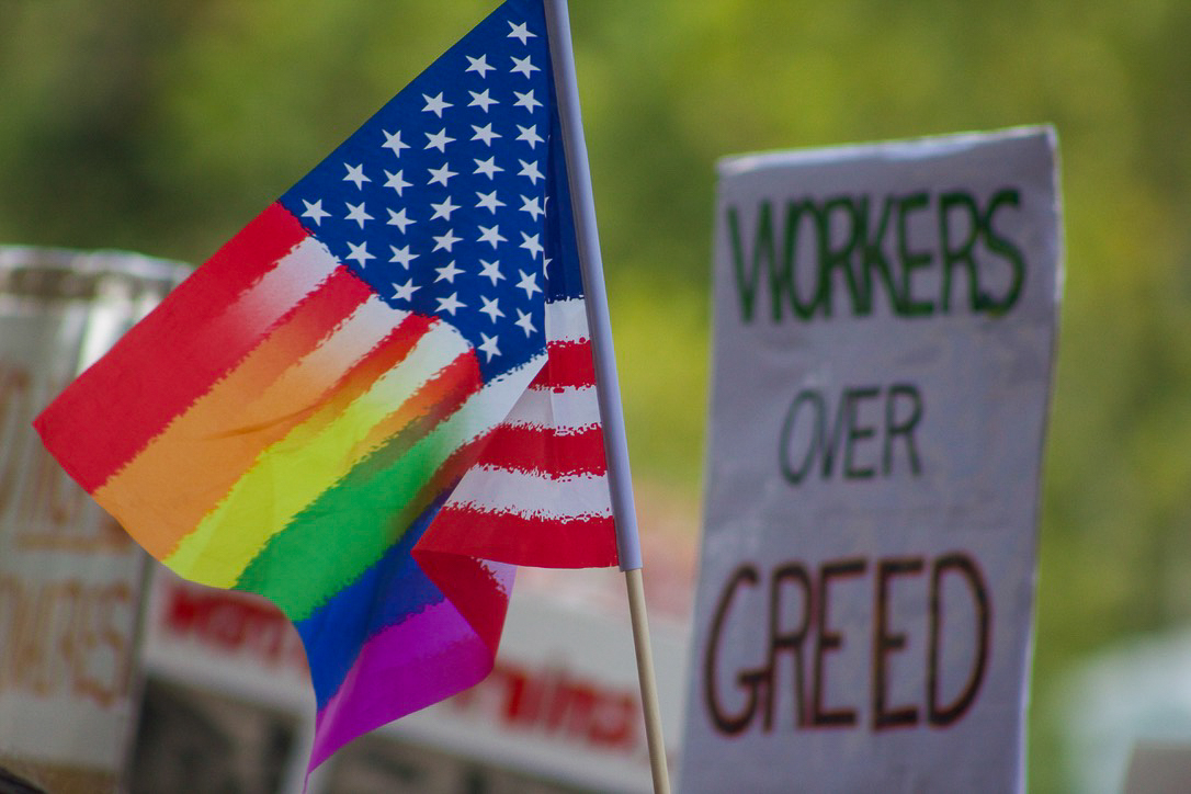 Rainbow American flag waves amongst demonstrator banners at the 'Workers Over Billionaires' protest located near the Kent gazebo on Monday, Sept. 1, 2025.