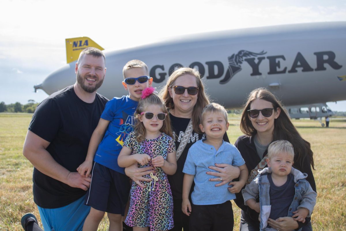 Zakary (left) and Stephanie Raynish (middle) poses for a picture with their two kids, Carter and Audrey Raynish (left), and their friend Alyssa Henry (right) and her two kids, Charlie and Jones (middle) in front of the Goodyear Blimp during the Aeronautics and Engineering Expo on Saturday, Sept 6, 2025.
