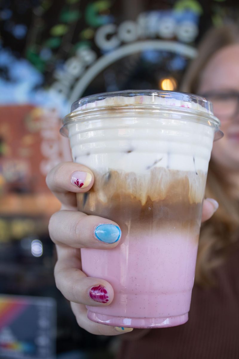 Emily Day, a sophomore speech pathology and audiology major, holds up the Her Latte in front of Scribbles Coffee Company on Saturday, Oct. 18, 2025. Her Campus teamed up with the coffee shop to make a drink in honor of Breast Cancer Awareness Month.
