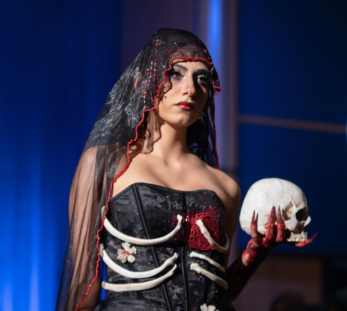 Kent student model TJ Chaccour holds a fake skull as she poses to show off her outfit during the Modista X Phi Delta Epsilon Fashion Show on Saturday, Oct. 18, 2025. She is wearing Taylor Allen and Reina Cirota's design that they made for the show.